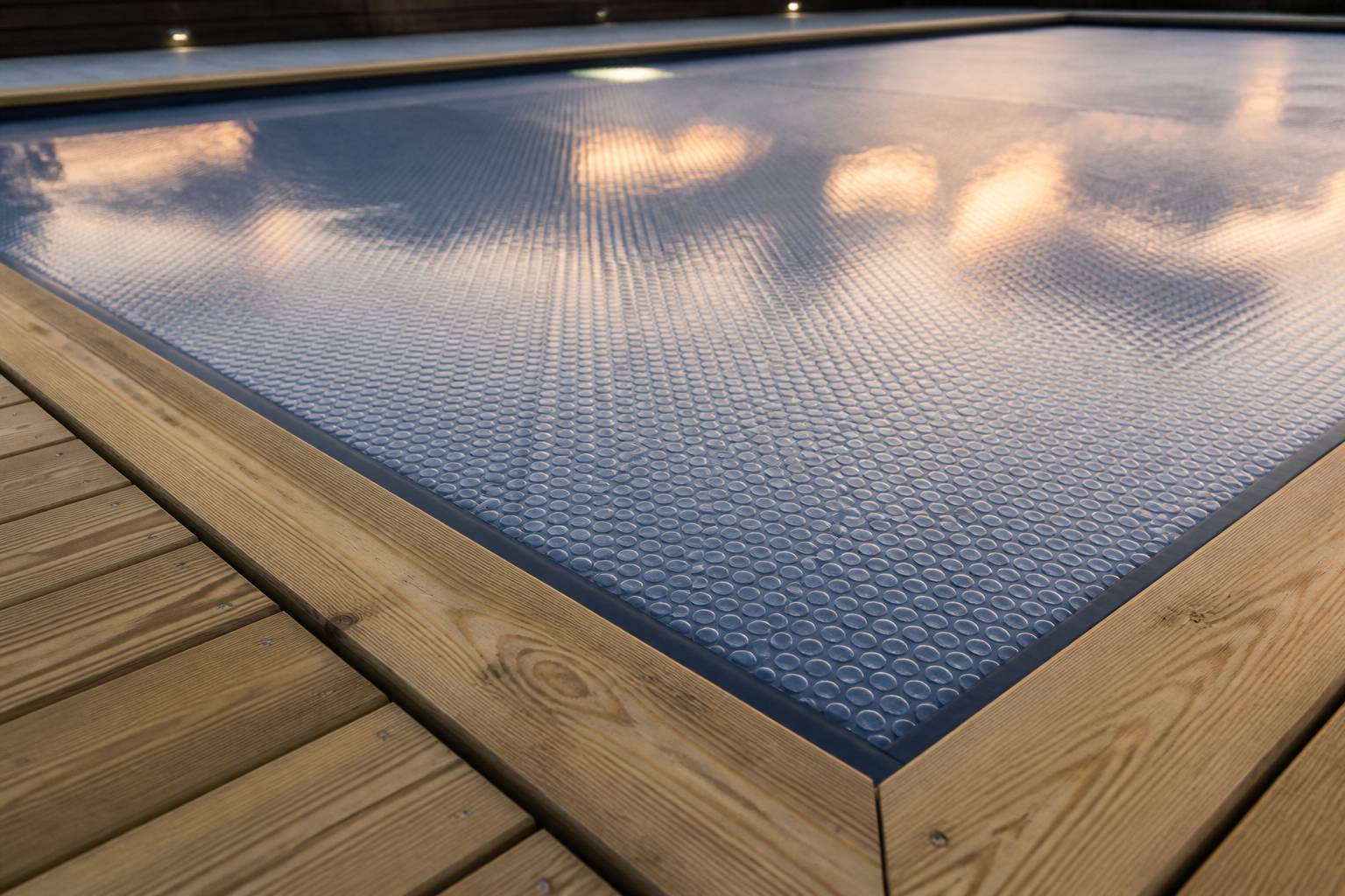 Gros plan sur une bâche à bulles posée sur l'eau d'une piscine avec des reflets du soir