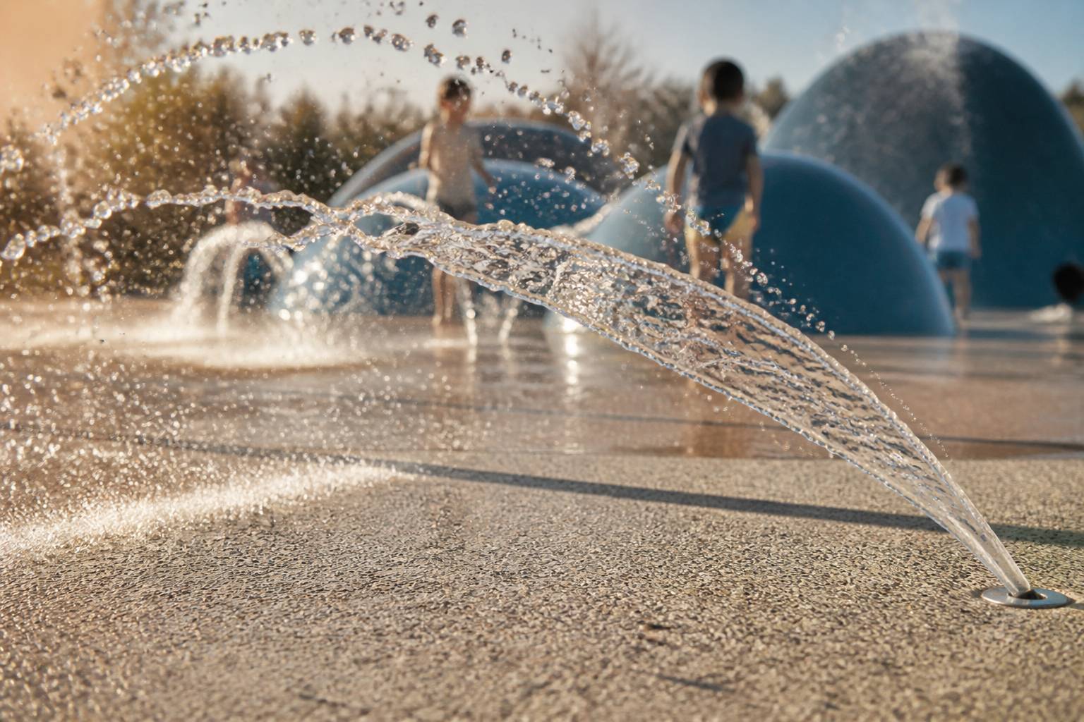 Jet d'eau en arche au-dessus d'un sol en béton désactivé avec structure de jeu arrondie bleue